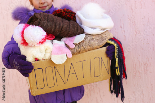 Girl holding donation box with warm winter clothes.