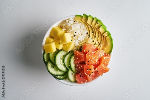 poke bowl with salmon, avocado, mango, rice, cucumbers, sprinkled with white and black sesame isolated on white background. top view