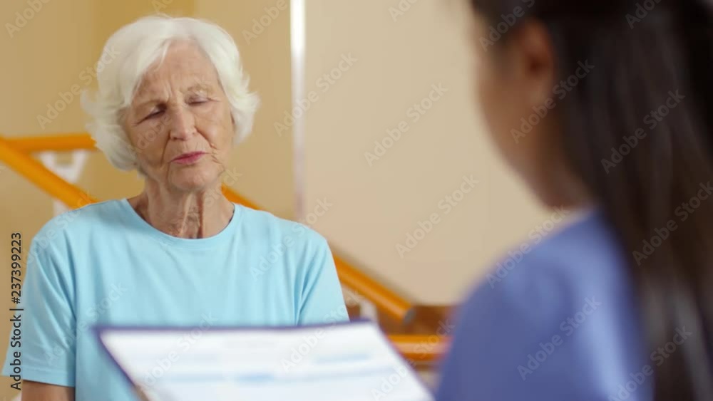 Medium shot of elderly woman having conversation with unrecognizable female physical therapy specialist with clipboard Medium shot of elderly woman having conversation with unrecognizable female physical therapy specialist with clipboard