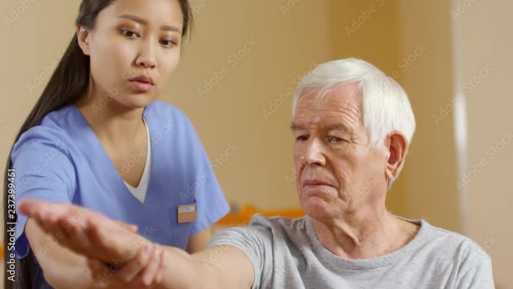 Medium shot of young female physiotherapist talking and stretching arm of elderly patient Medium shot of young female physiotherapist talking and stretching arm of elderly patient