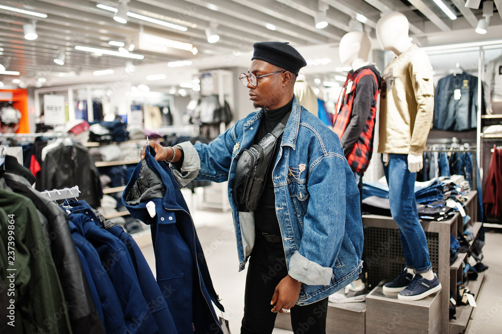 Stylish casual african american man at jeans jacket and black beret at clothes store looking on new jacket.