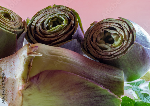 group of cut artichokes ready to cook with mint plant on pink color background