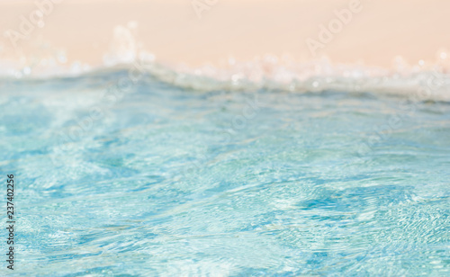 Bokeh blurred soft azur sea water wave and light pure sand on the beach. Vacation theme background.