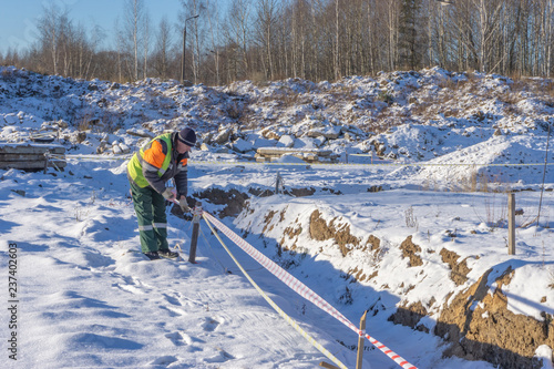 A worker at a construction site shields trenches with a signal tape for cadastral surveying.
