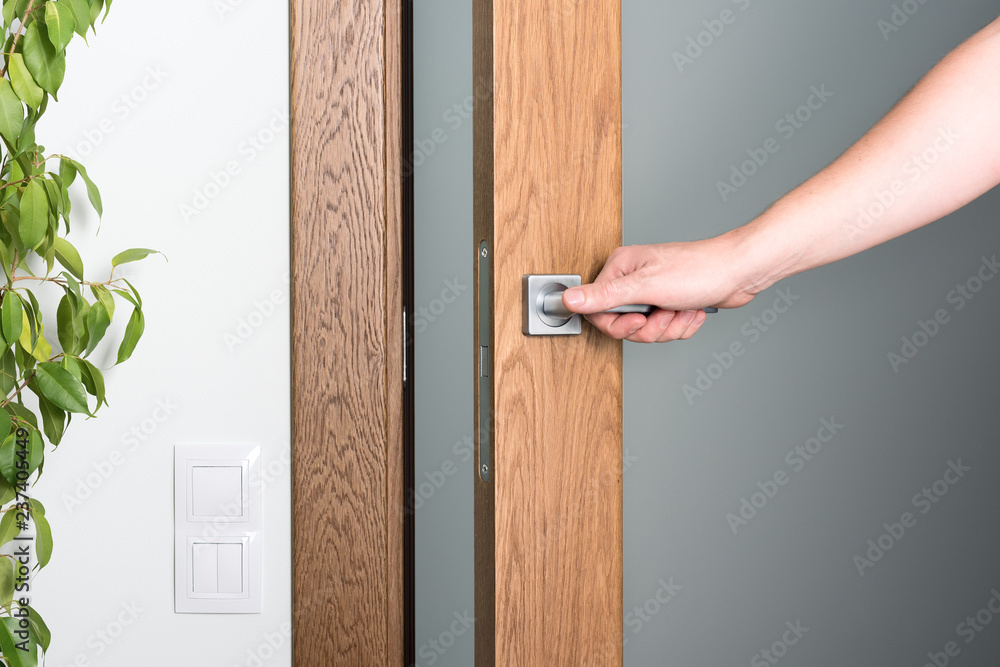 Fototapeta premium Open the door. A man's hand on the door handle. Dark wood and light interior.