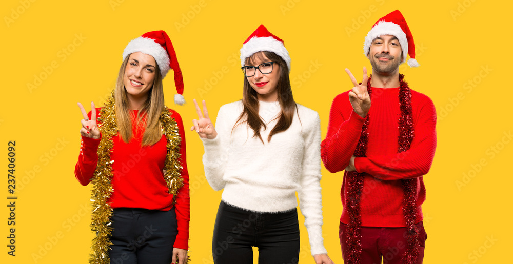 Fototapeta premium A group of people Blonde woman dressed up for christmas holidays happy and counting two with fingers on yellow background