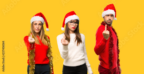 A group of people Blonde woman dressed up for christmas holidays making horn gesture. Negative expression on yellow background