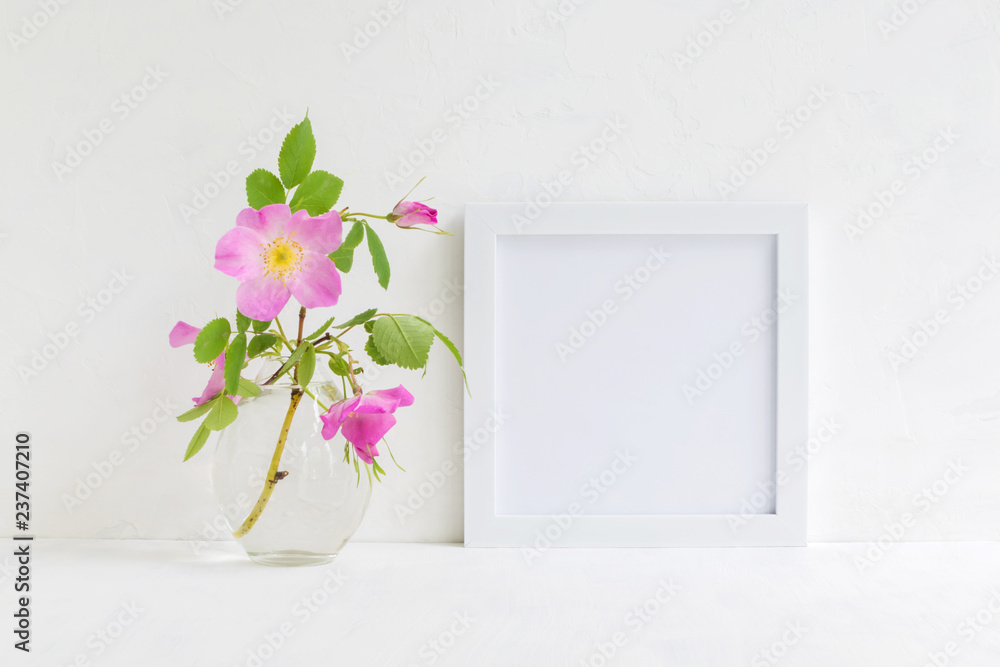 Mockup with a white frame and pink rose hips flowers Mockup with a white frame and pink rose hips flowers