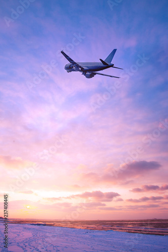Airplane in the sky over the snowy beach at sunset