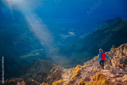 Female tourist with red backpack running in mountains. Orange sunset light in background