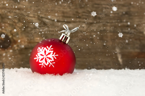 Red Christmas ball in snow on wooden background