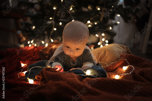 Baby in a sweater next to Christmas tree  festive