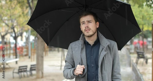 Front view portrait of a frustrated man walking in a park complaining about bad weather in a rainy day of winter