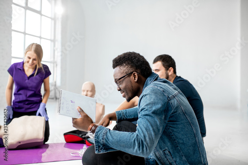 Man having a question during the first aid courses with instructors showing some practise on medical dummies in the white room