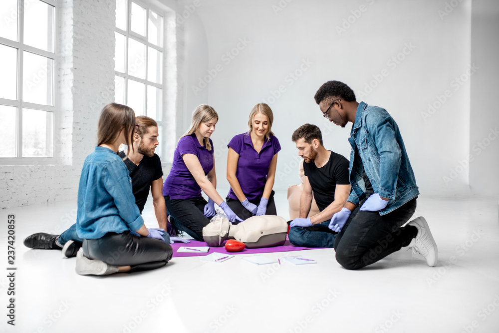 Group of young people learning to make artificial breathing with medical dummies during the first aid training in the white room Group of young people learning to make artificial breathing with medical dummies during the first aid training in the white room
