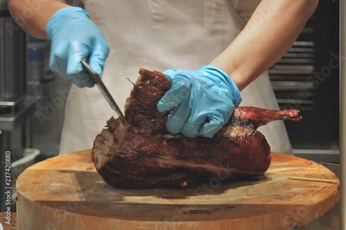 Man hand wear blue rubber glove holding Grill Roasted Peking Duck and cleaver on round wooden Chopping board in the kitchen