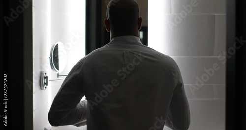 Young man in bathroom mirror putting his shirt on photo