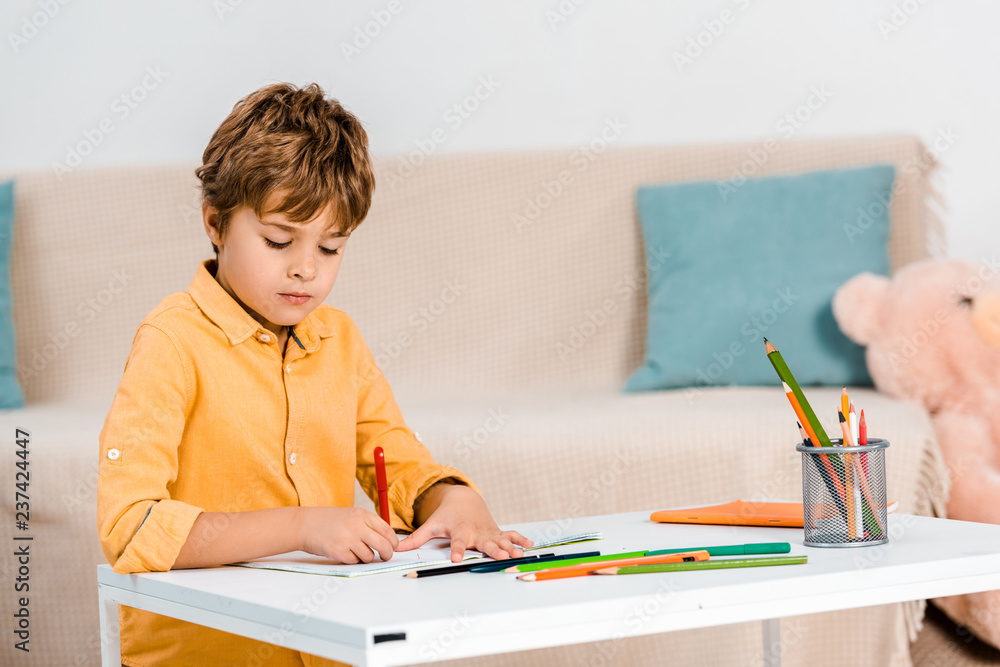 focused boy writing with pen and studying at table at home focused boy writing with pen and studying at table at home