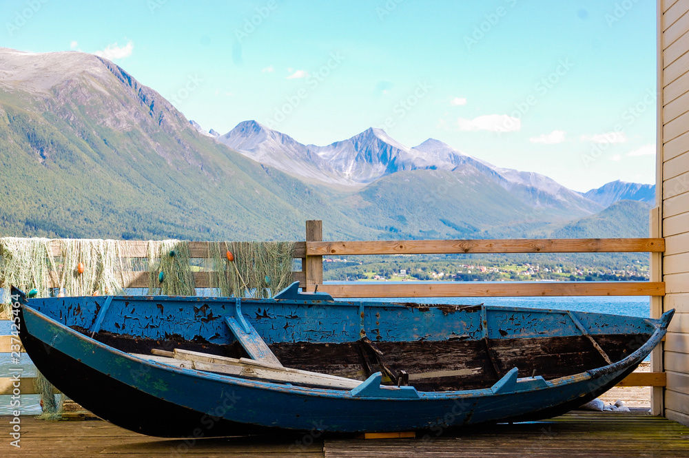 Old little blue boat and a fishing net in picturesque and colorful Norwegian town scenery; fjord background