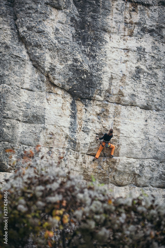 woman climbs grey-color rock in orange pants, back view