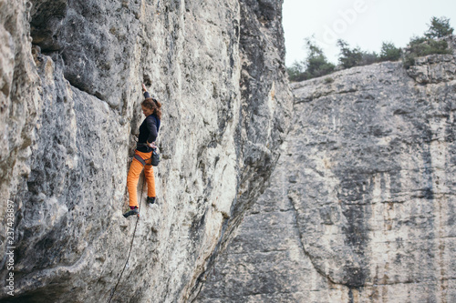 woman climbs grey-color rock in orange pants