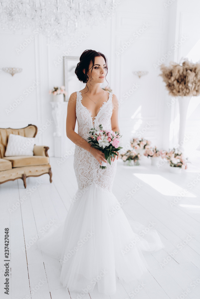 A bride in a white dress is holding a beautiful wedding bouquet. The bride is waiting for the groom in the white room. A bride in a white dress is holding a beautiful wedding bouquet. The bride is waiting for the groom in the white room.