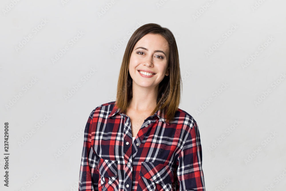 Smiling positive female with attractive look, wearing checkered shirt, posing against white blank wall Smiling positive female with attractive look, wearing checkered shirt, posing against white blank wall