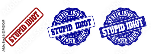 STUPID IDIOT scratched stamp seals in red and blue colors. Vector STUPID IDIOT marks with scratced style. Graphic elements are rounded rectangles, rosettes, circles and text tags.