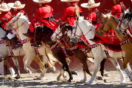 Group of mexican escaramuza girls with red mexican dresses and sombrero ride horseback on a rodeo photo