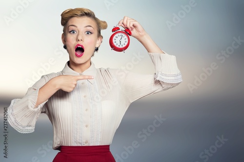 Shocked woman with alarm clock on blurred interior background