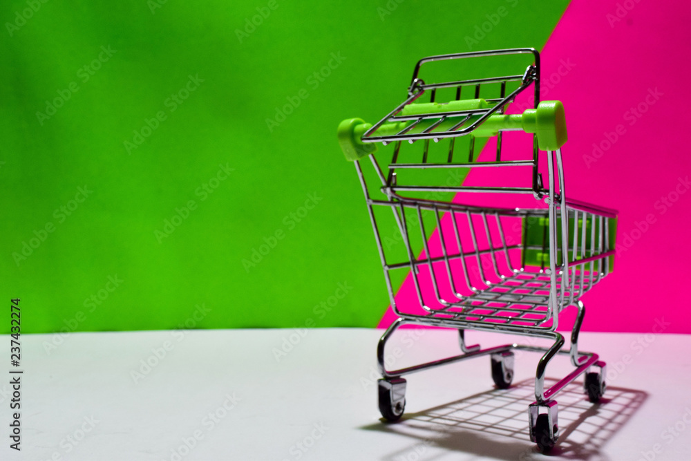 Empty green shopping cart isolated on green and pink background. E-commerce and business marketing concept