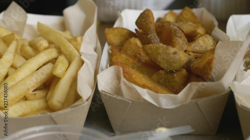 Detail shot of the of tray with fried chicken, french fries, ketchup and cheese sauce in city cafe. Woman's fingers dip food in sauces.