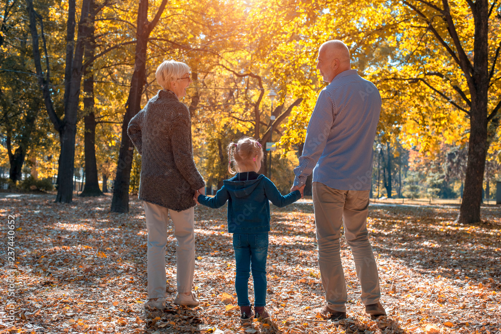 Happy grandparents and grandchild walking in autumn park together