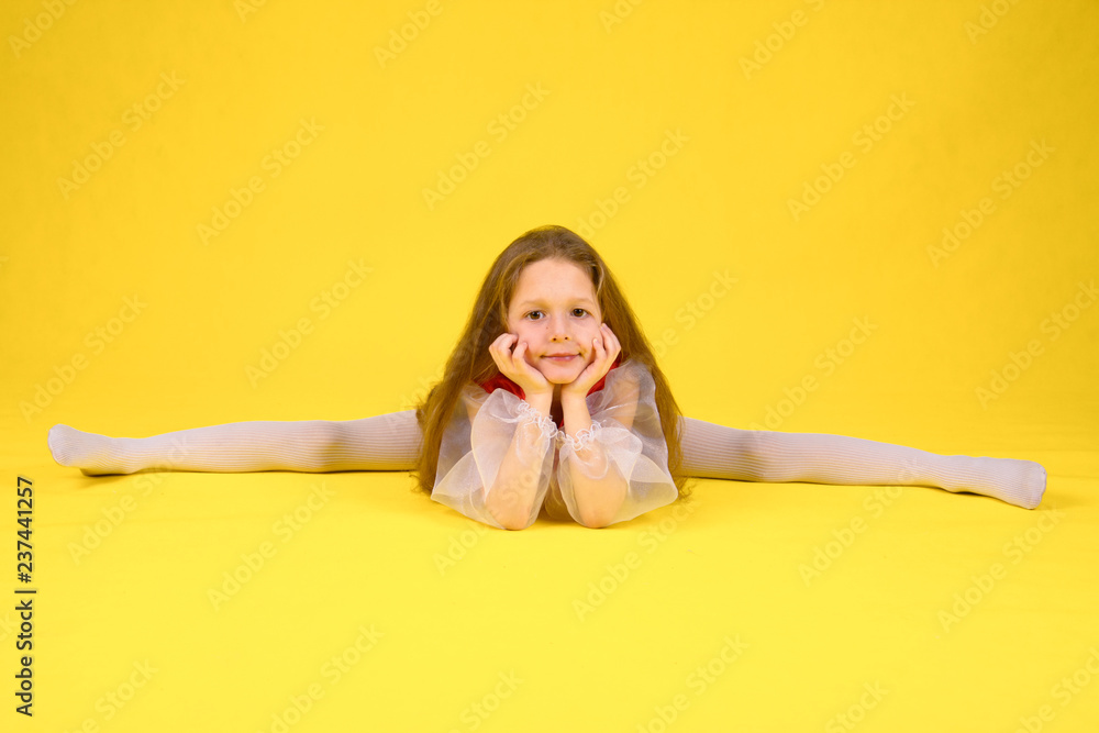 The child shows the class and sits on the splits. Yellow background. Girl with long hair in a stylized red dress The child shows the class and sits on the splits. Yellow background. Girl with long hair in a stylized red dress