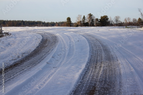 Turn of beautiful rural dirt road under snow, track in a field with forest on the horizon - rural landscape, travel trip