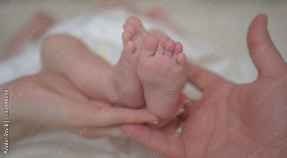 Newborn. Small legs in the hands of father and mother. Love and parenthood. A gentle photo of happy moments. Family concept. Newborn. Small legs in the hands of father and mother. Love and parenthood. A gentle photo of happy moments. Family concept.