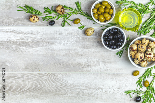 Set of black and green olives, quail eggs on plates, olive oil and rosemary