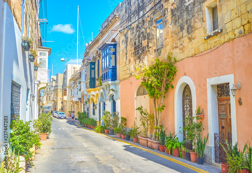 The scenic street with old stone residential house with blue Maltese balconies and plants in pots along its walls, Naxxar, Malta photo