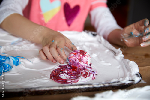 Girl swirls an easter egg in purple dye and shaving cream photo