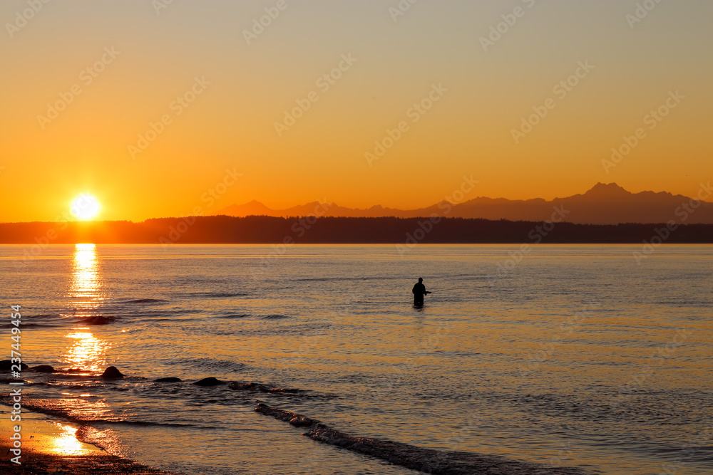 A lone fisherman fishing during a sunset at Golden Gardens Park, Seattle Washington 