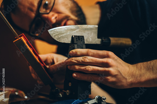 Mann schärft ein japanisches Küchenmesser an einem modernen Schleifwerkzeug photo