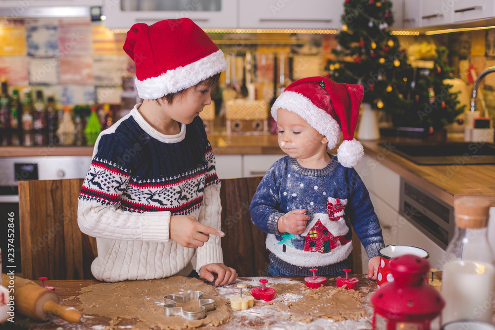 Sweet toddler child and his older brother, boys, helping mommy preparing Christmas cookies at home Sweet toddler child and his older brother, boys, helping mommy preparing Christmas cookies at home