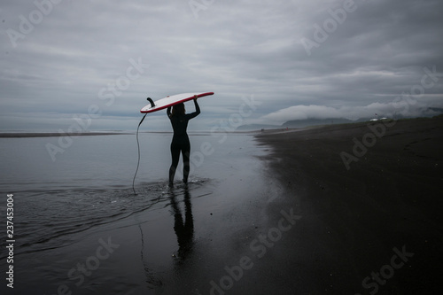 Surfing on the black volcanic beach of the Pacific Ocean, Kamchatka, Russia, the Far East. Extreme sport in cold water.
