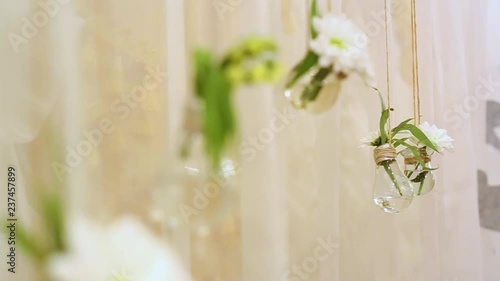 Wedding unusual floral decoration inside of transparent glass mini vases. Small cute bouquets of white fresh flowers hanging from ceiling isolated on fabric background. Details of wedding photobooth.