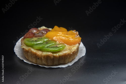 fruit tart stacked high with kiwi peach grape dark background.