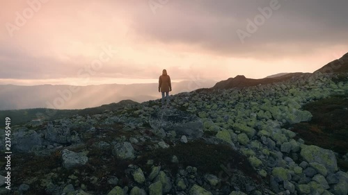 Woman standing on rock on top of the high mountain looking epic view in Norway at sunset aerial shot photo