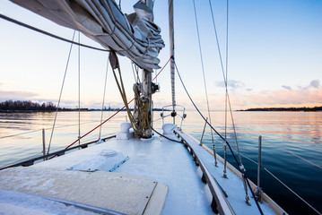 Colorful winter sunset. White yacht sailing, a view from the deck to the bow and sails. Baltic sea, Latvia