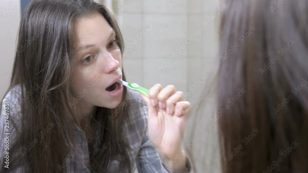 Sleepy woman brushing her teeth in the bathroom in front of the mirror. Sleepy woman brushing her teeth in the bathroom in front of the mirror.