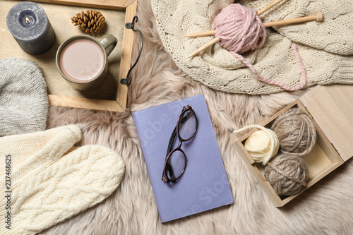 Flat lay composition with book, wool balls and cup of coffee on fuzzy rug