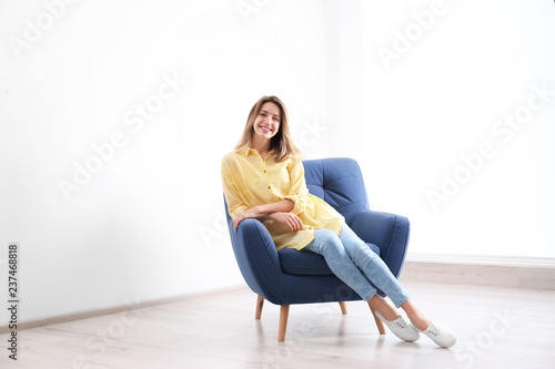 Young woman sitting in armchair at home. Space for text